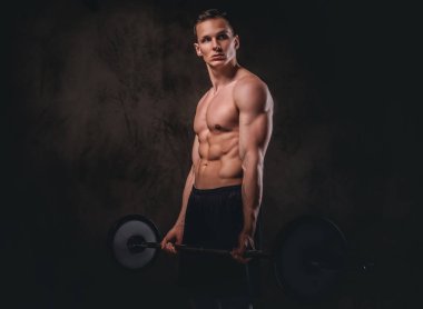 Bir halter tutarak ve pazı üzerinde egzersiz yaparak genç gömleksiz vücut geliştiricisi. Koyu arka plan üzerinde izole.