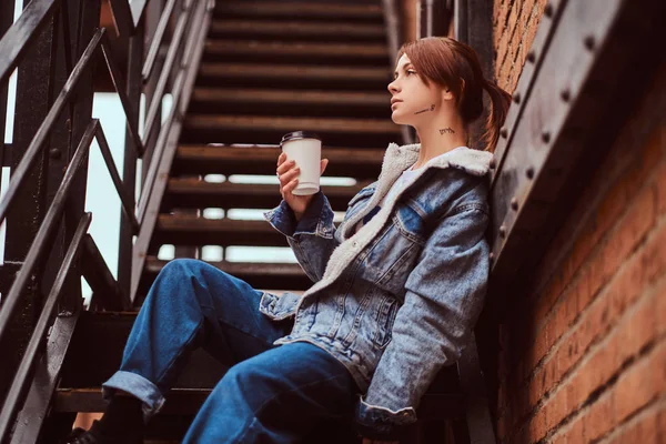 Kafe dışında merdivenlerde oturan ve paket servisi olan restoran kahve tutan trendy kıyafetler giymiş güzel bir kız. — Stok fotoğraf