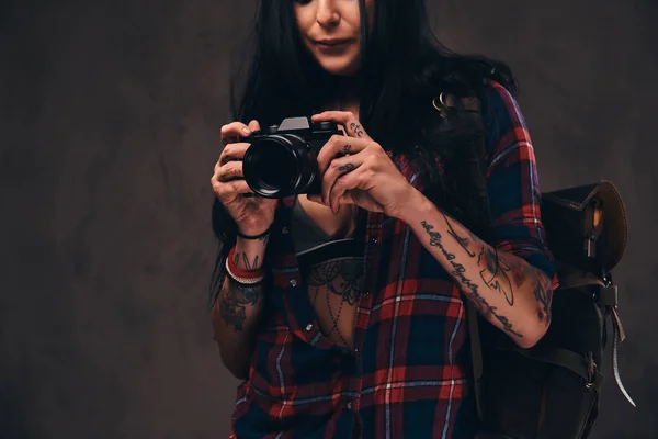 Tatuato hipster ragazza indossa una camicia rossa a quadri sbottonata che tiene una fotocamera su uno sfondo scuro . — Foto Stock