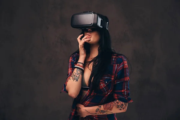Tattooed girl wearing a red unbuttoned checked shirt wearing a VR headset.
