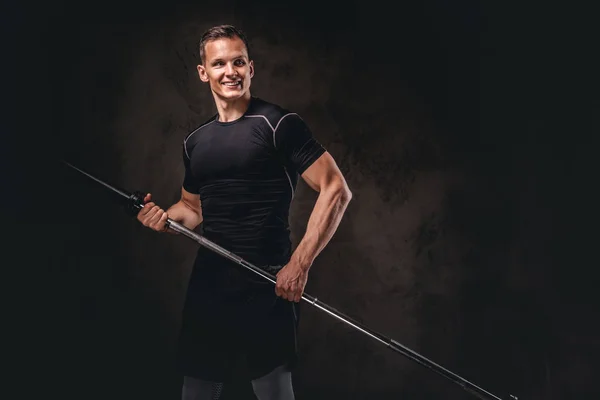 Retrato de um belo jovem fisiculturista segurando um sino e olhando para o fundo escuro . — Fotografia de Stock