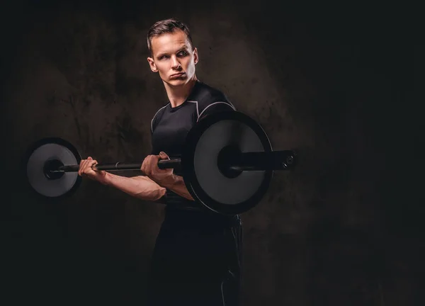 Konzentrierter junger Sportler, der eine Langhantel in der Hand hält und Übungen auf dem Bizeps macht. isoliert auf dunklem Hintergrund. — Stockfoto