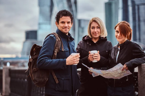 Ομάδα χαμογελώντας τουριστών, κρατώντας τον χάρτη και takeaway καφέ μπροστά από ουρανοξύστες — Φωτογραφία Αρχείου