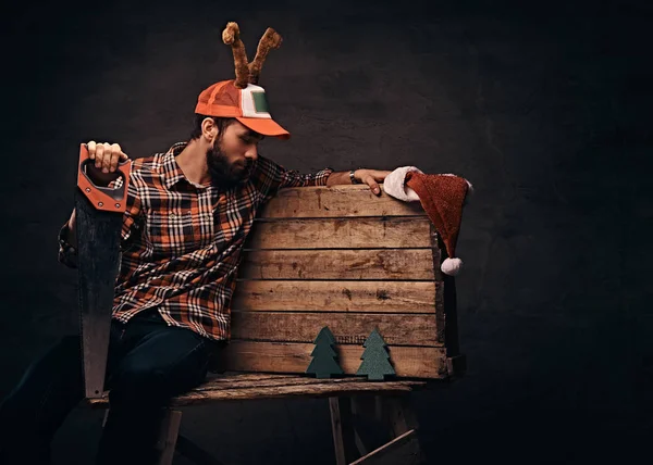 Carpintero con gorra de navidad decorada sentado en una paleta de madera . — Foto de Stock