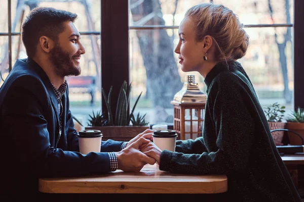 Atractiva pareja joven tomados de la mano, mirándose y hablando mientras están sentados en el restaurante . — Foto de Stock