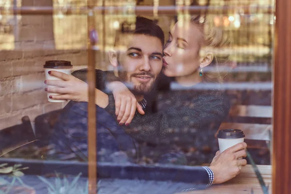 Beautiful girl sitting on her boyfriends lap on the cafe behind the window. — Stock Photo, Image