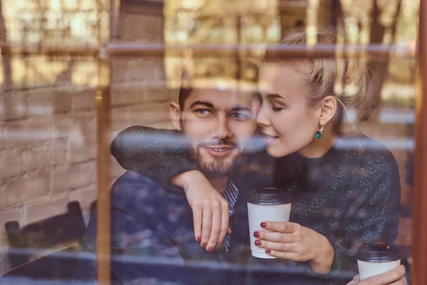 Mooi meisje zittend op de schoot van haar vriendjes op het cafe achter het venster. — Stockfoto