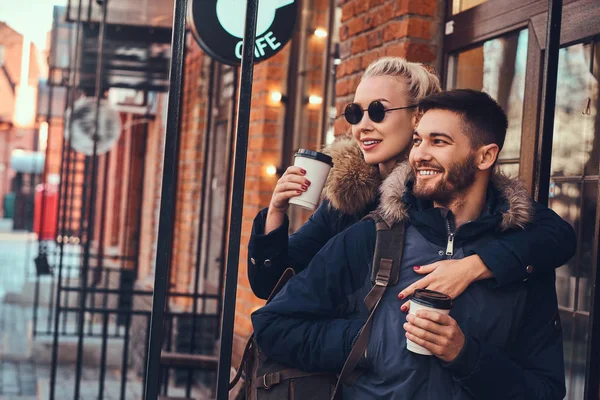 Una hermosa chica abraza a su novio cerca de la cafetería afuera . — Foto de Stock