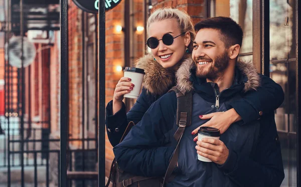 Una hermosa chica abraza a su novio cerca de la cafetería afuera . — Foto de Stock