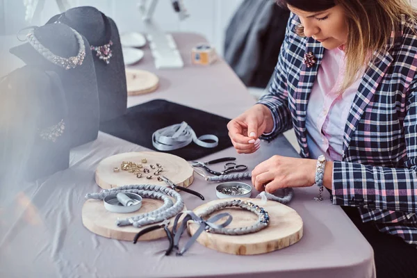 Mujer elegantemente vestida hace collares hechos a mano, trabajando con agujas e hilo en el taller . — Foto de Stock