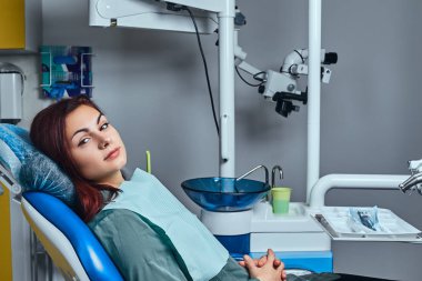 Bir dişçi ofisinde bir sandalyede oturan genç kadın.