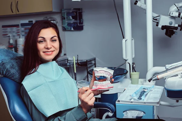 Giovane donna felice che tiene uno spazzolino da denti e una dentiera in uno studio dentistico . — Foto Stock