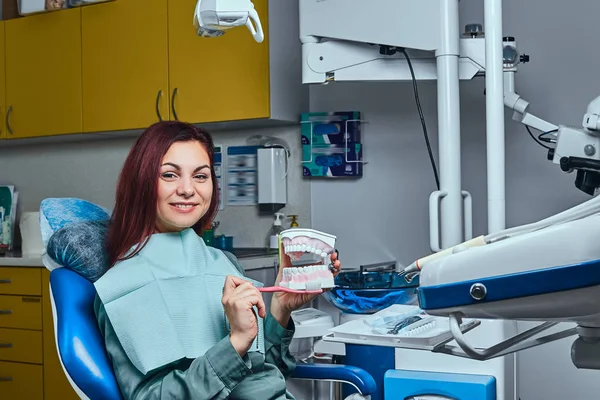 Giovane donna felice che tiene uno spazzolino da denti e una dentiera in uno studio dentistico . — Foto Stock