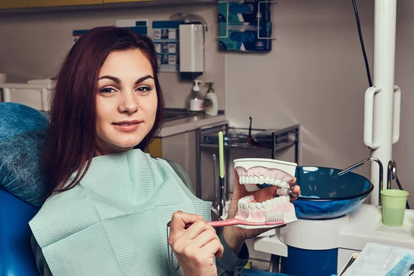 Młoda kobieta siedzi w fotelu u dentysty i przytrzymując protezy w gabinecie stomatologicznym. — Zdjęcie stockowe