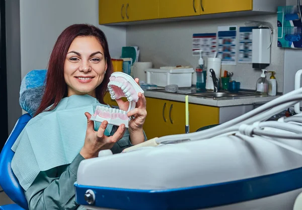 Młoda Ruda kobieta siedzi w fotelu u dentysty i przytrzymując protezy w gabinecie stomatologicznym. — Zdjęcie stockowe