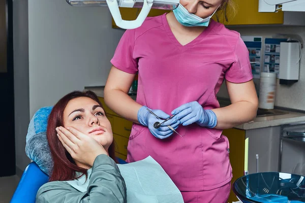 Mulher ruiva jovem que sofre de uma dor de dente enquanto se senta em uma cadeira no escritório do dentista . — Fotografia de Stock