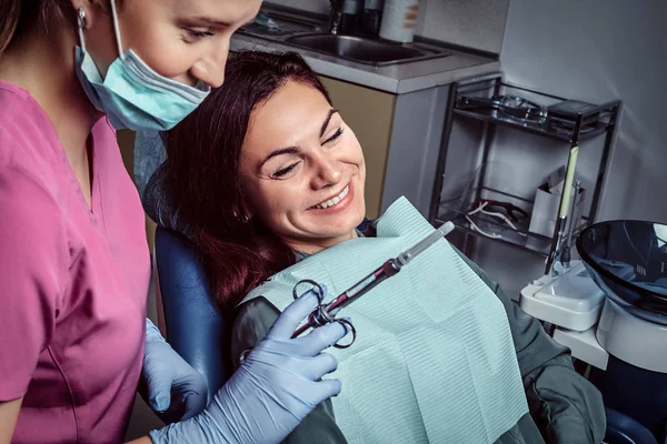 Patientin sitzt im Zahnarztstuhl, während sich ihr Arzt auf die Spritze vorbereitet. — Stockfoto
