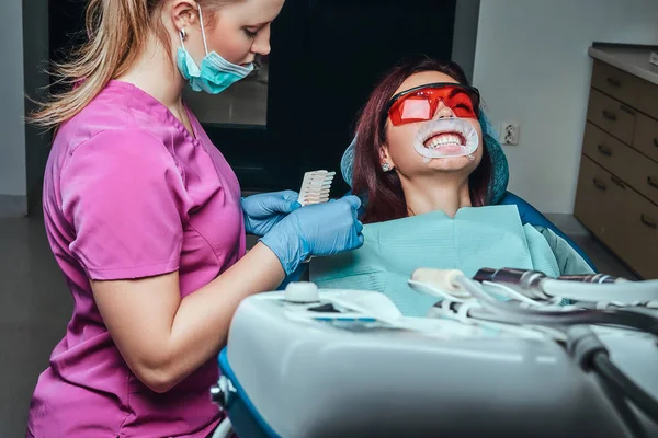 女性歯科医がホワイトニングの歯科医のオフィスで歯科医色のレベルをチェックします。. — ストック写真