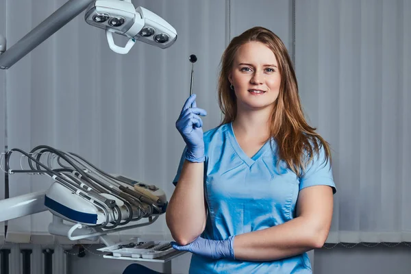 Sorridente dentista femminile in possesso di specchio dentale mentre in piedi nel suo studio dentista . — Foto Stock