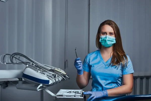 Dentista feminina segurando espelho dental enquanto sentada em seu consultório odontológico . — Fotografia de Stock