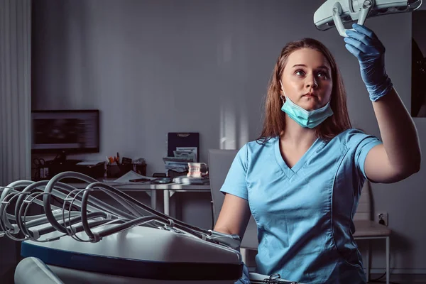 Жінка-стоматолог коригує освітлювальне обладнання над стільцем у стоматологічній клініці . — стокове фото