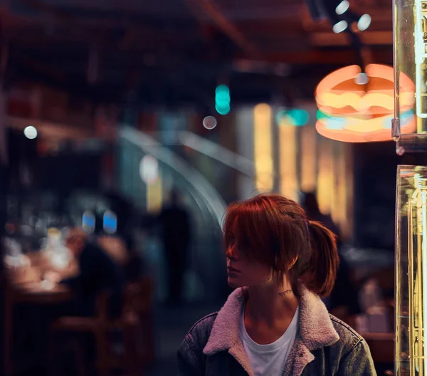 Стильная рыжая девушка, стоящая ночью на улице. Иллюминированные вывески, неон, огни . — стоковое фото