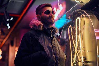 Yakışıklı bir adam sokakta gece ayakta ceplerinde bir ceket ve elleri ile güneş gözlüğü giyiyor. 