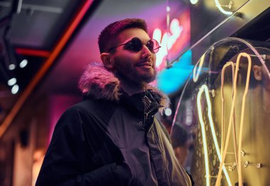 Yakışıklı bir adam sokakta gece ayakta ceplerinde bir ceket ve elleri ile güneş gözlüğü giyiyor. 