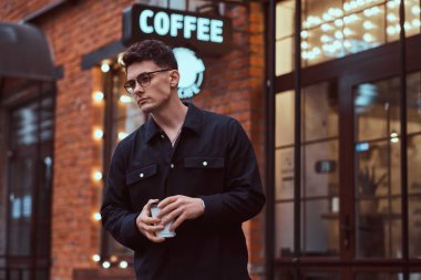 Bir paket kahve dışında bir kafe yakın dururken tutan bir yakışıklı delikanlı.