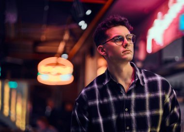 Gece sokakta duran yakışıklı bir genç adam. Işıklı tabela, neon, ışıklar.