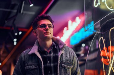 Genç bir adam sokakta geceleri ayakta modaya uygun giyinmiş. Işıklı tabela, neon, ışıklar.