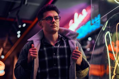 Genç bir adam sokakta geceleri ayakta modaya uygun giyinmiş. Işıklı tabela, neon, ışıklar.