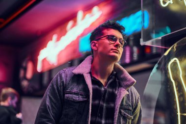 Genç bir adam sokakta geceleri ayakta modaya uygun giyinmiş. Işıklı tabela, neon, ışıklar.