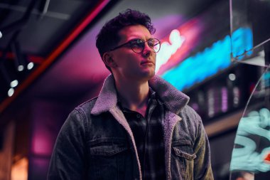 Genç bir adam sokakta geceleri ayakta modaya uygun giyinmiş. Işıklı tabela, neon, ışıklar.