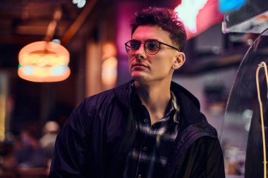 Gece sokakta duran yakışıklı bir genç adam. Işıklı tabela, neon, ışıklar.