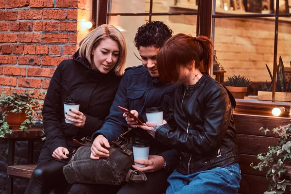 Three happy friends having a break with coffee sitting near a cafe outside. — Stock Photo, Image