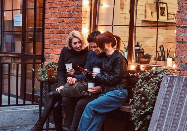 Three happy friends having a break with coffee sitting near a cafe outside. — Stock Photo, Image