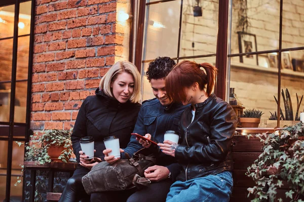 Three happy friends having a break with coffee sitting near a cafe outside.