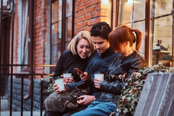 Tre glada vänner som har en paus med kaffe sitter nära ett café utanför. — Stockfoto