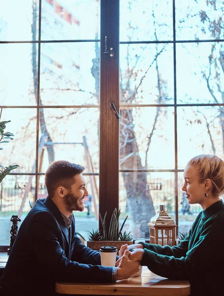 Attraente giovane coppia che si tiene per mano, si guarda e parla mentre si siede al ristorante . — Foto Stock