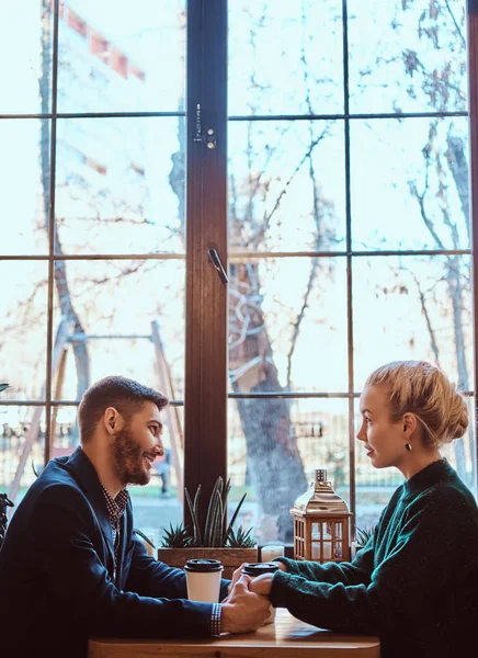 Attractive young couple holding hands, looking at each other and talking while sitting in the restaurant.