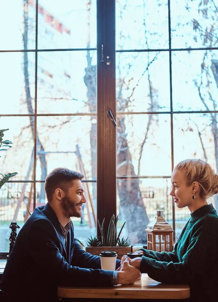 Attraente giovane coppia che si tiene per mano, si guarda e parla mentre si siede al ristorante . — Foto Stock