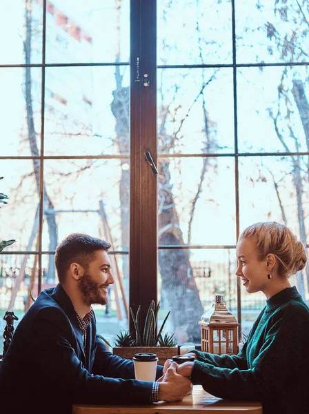 Attractive young couple holding hands, looking at each other and talking while sitting in the restaurant.