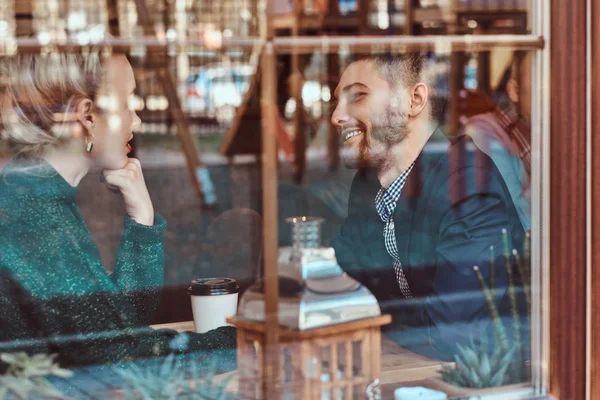 Aantrekkelijke jonge paar kijken naar elkaar en praten tijdens de vergadering in het restaurant achter het venster. — Stockfoto