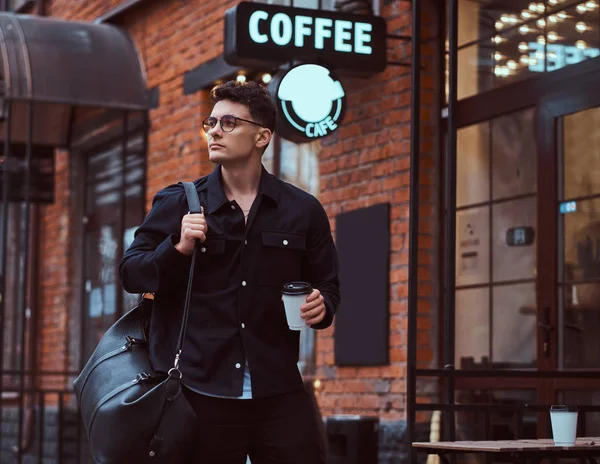 Egy jóképű fiatalember gazdaság egy elvihető kávé állva közelében egy kávézó a szabadban. — Stock Fotó