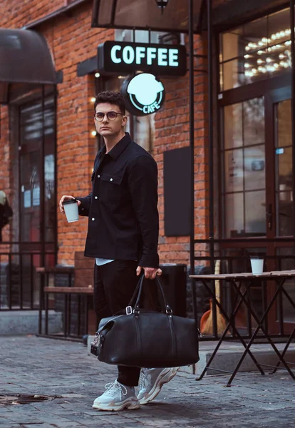 Egy jóképű férfi, szemüveget viselt ing gazdaság elvihető kávé és táska rövid idő gyaloglás legyőz a utca. — Stock Fotó