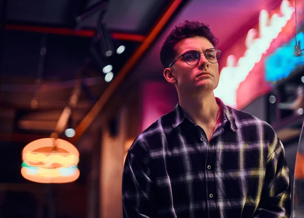 Un joven guapo de pie por la noche en la calle. Letreros iluminados, neón, luces . — Foto de Stock