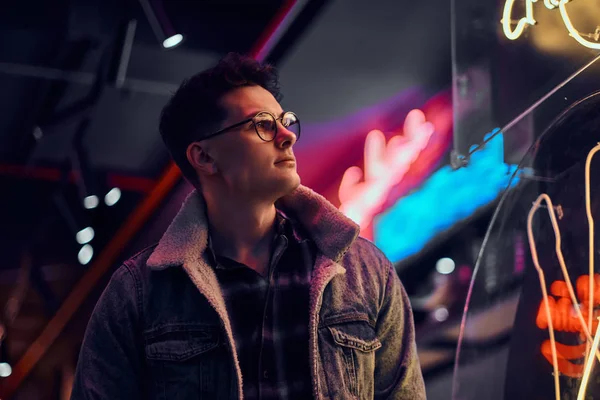 Un joven vestido a la moda de pie en la calle por la noche. Letreros iluminados, neón, luces . — Foto de Stock