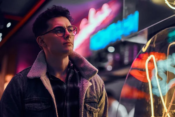 A young man fashionably dressed standing in the street at night. Illuminated signboards, neon, lights. — Stock Photo, Image