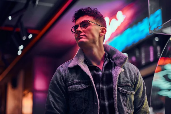 Un joven vestido a la moda de pie en la calle por la noche. Letreros iluminados, neón, luces . — Foto de Stock